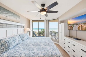 Ein Schlafzimmer mit Bett, Deckenventilator, Fernseher, Balkon mit Meerblick und einem Bild an der Wand.