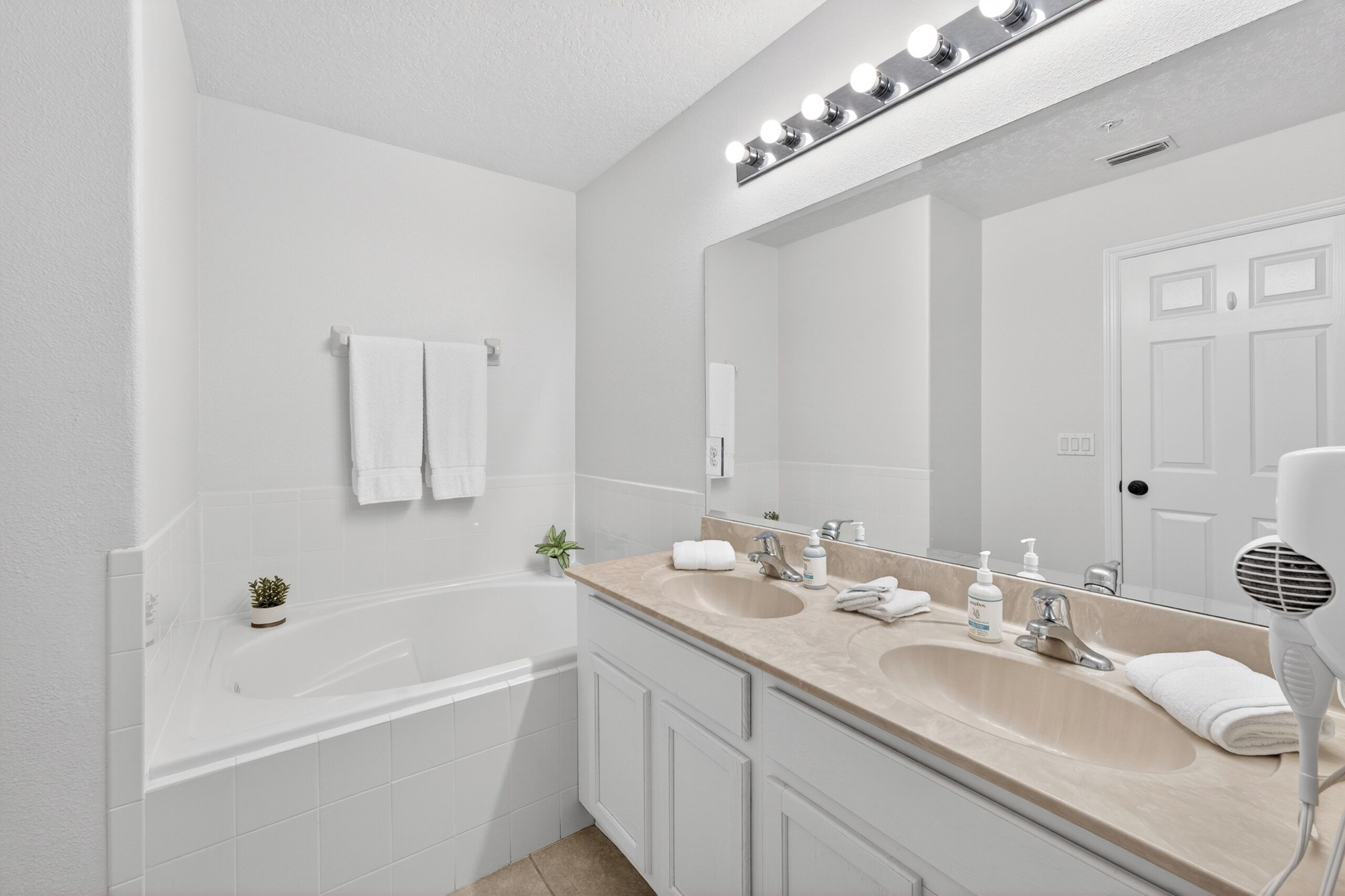 A bathroom with a bathtub, two sinks, a large mirror, and a hairdryer.
