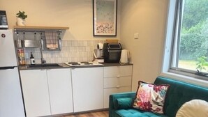 Una cocina compacta con armarios blancos, un sofá verde azulado, una mesa de centro de madera y una ventana con vistas a la vegetación.