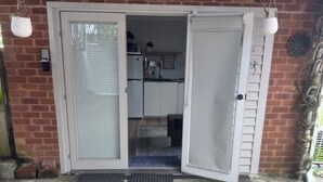 Un espacio al aire libre techado con suelo de hormigón, una puerta blanca que da a una cocina y un muro de ladrillo.