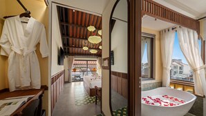 A hotel room with a large bathtub, a wooden ceiling, a view through a window, and a hallway leading to a dining area.