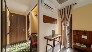A hotel room with a wooden wardrobe, a small table with a vase, a wooden bench, and a mirror.