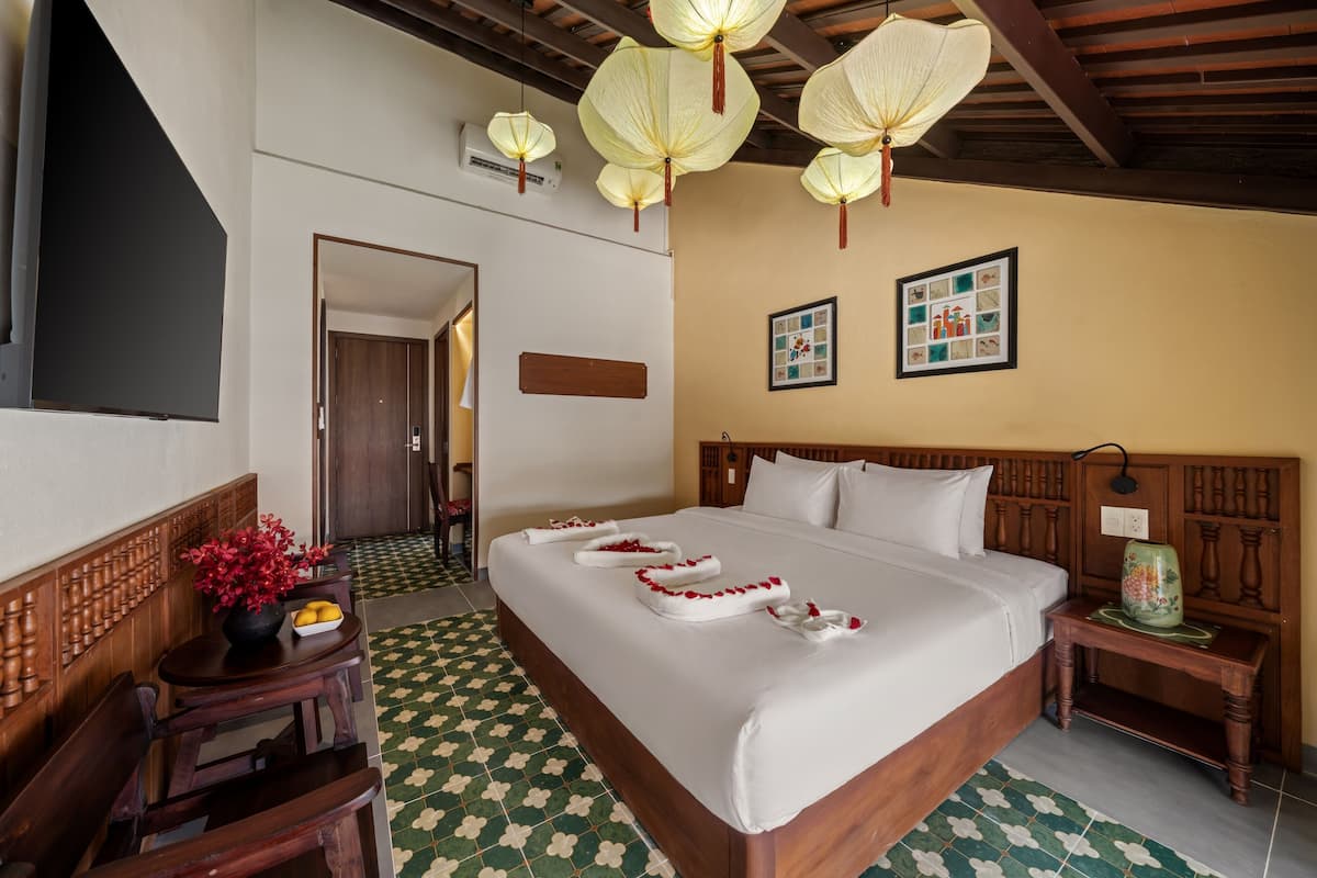 A hotel room with a large bed, wooden headboard, a small table with a vase, and a wall-mounted air conditioner.