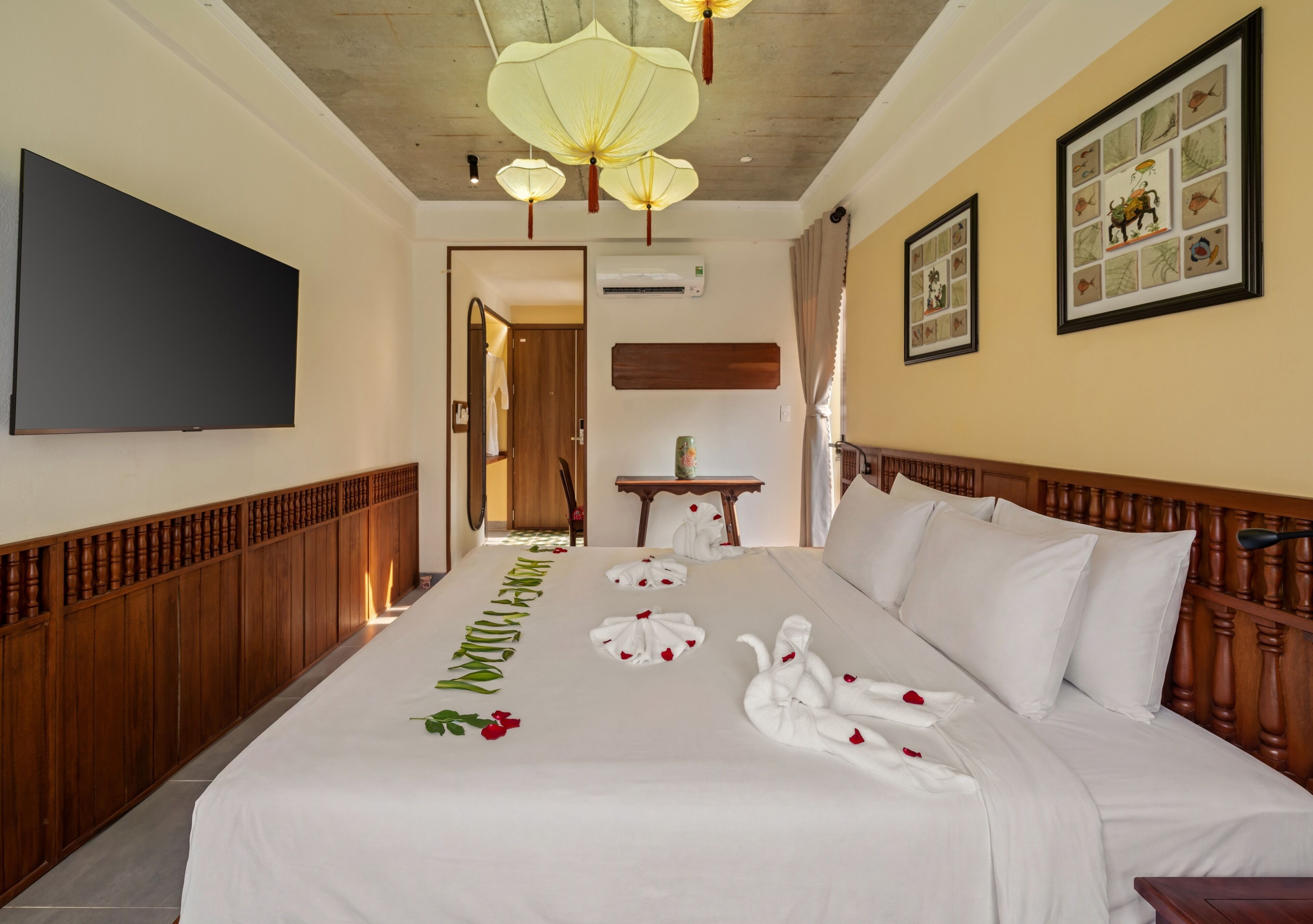 Quarto de hotel com cama grande, televisão de tela plana, cabeceira de madeira, arte decorativa na parede e ventilador de teto.