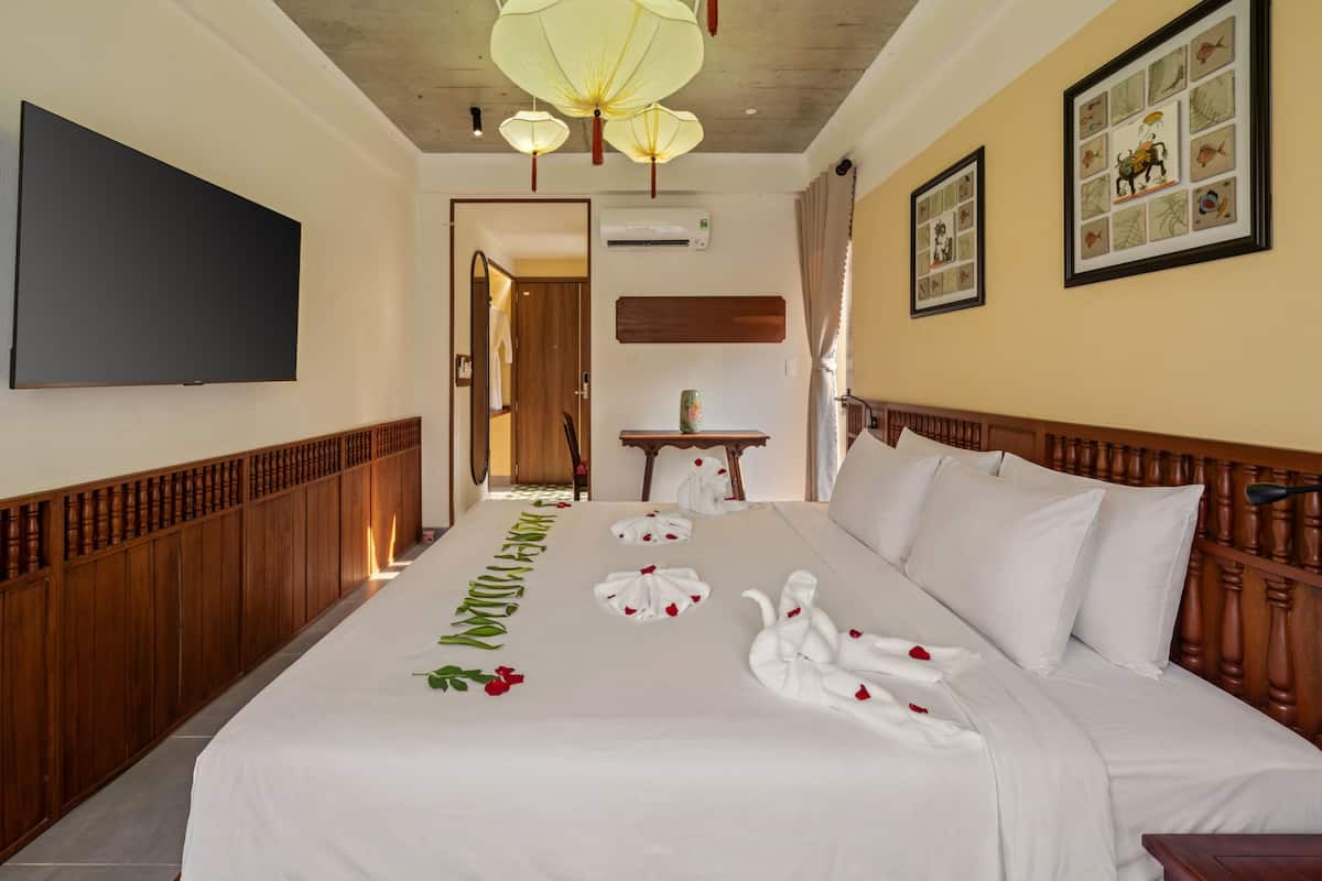 A hotel room with a large bed, a flat-screen TV, wooden headboard, decorative wall art, and a ceiling fan.