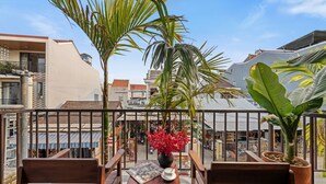 A balcony with wooden chairs, a table with a newspaper, and a potted plant with red flowers.