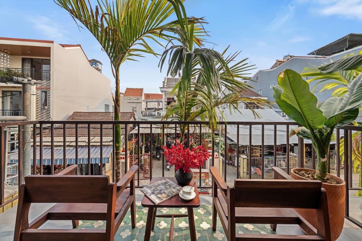 A balcony with wooden chairs, a table with a newspaper, and a potted plant with red flowers.