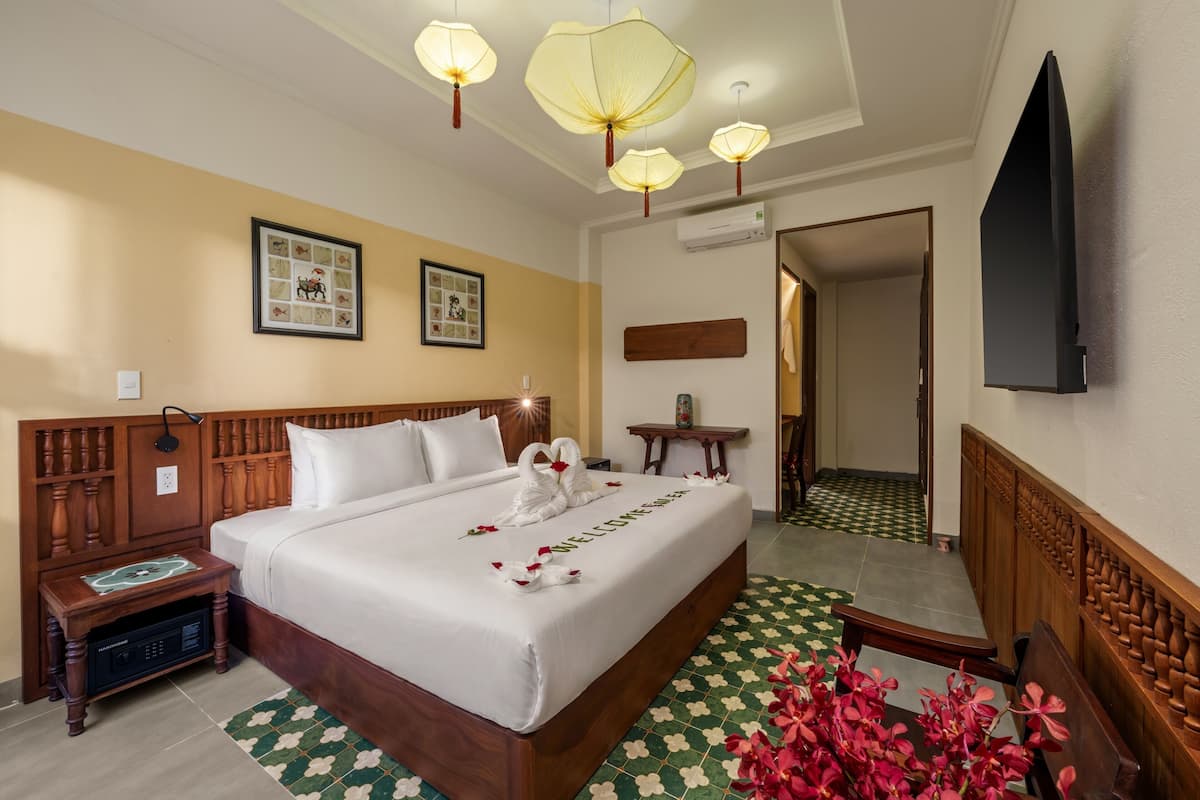 A hotel room with a large bed, a bedside table with a radio, a wall-mounted TV, and a framed picture on the wall.