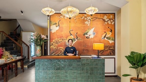 A reception desk with a large mural of cranes and flowers, a staircase, and a potted plant. - Solea Boutique Hoi An (Hoi An)