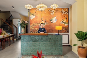Un comptoir d’accueil orné d’une grande fresque représentant des grues et des fleurs, un escalier et une plante en pot.