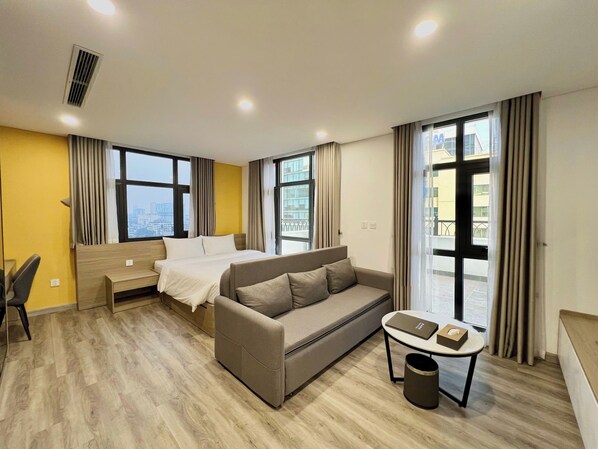 Habitación de hotel con cama, sofá, escritorio y ventanas amplias.