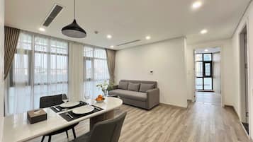 Una sala de estar moderna con sofá, mesa de comedor y sillas. Hay una ventana con cortinas, una lámpara en el techo y una puerta que conduce a otra habitación.