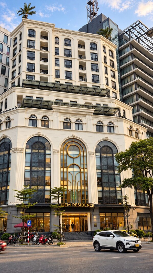 Un edificio de varios pisos con una entrada destacada, amplias ventanas en arco y un letrero que dice 'GEM RESIDENCE'.