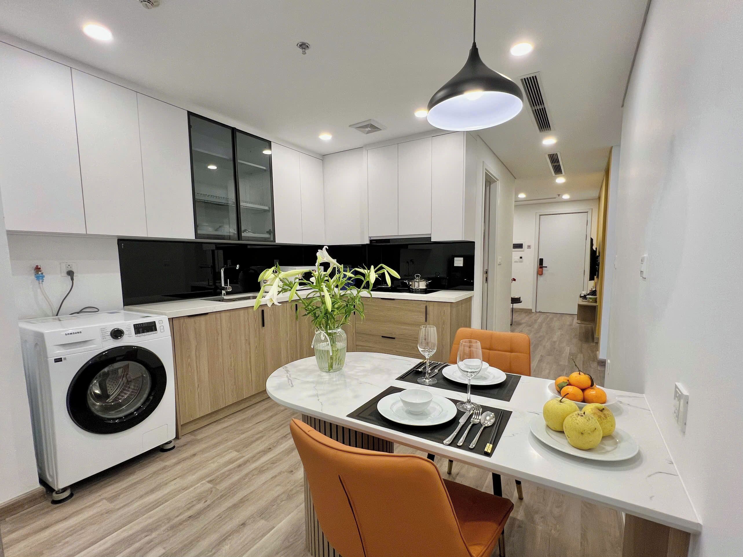 A modern kitchen with a built-in washer, a dining area with a table set for two, and a vase with flowers.