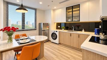 A modern kitchen with a built-in washer, a dining area with orange chairs, and a view of the city through large windows.