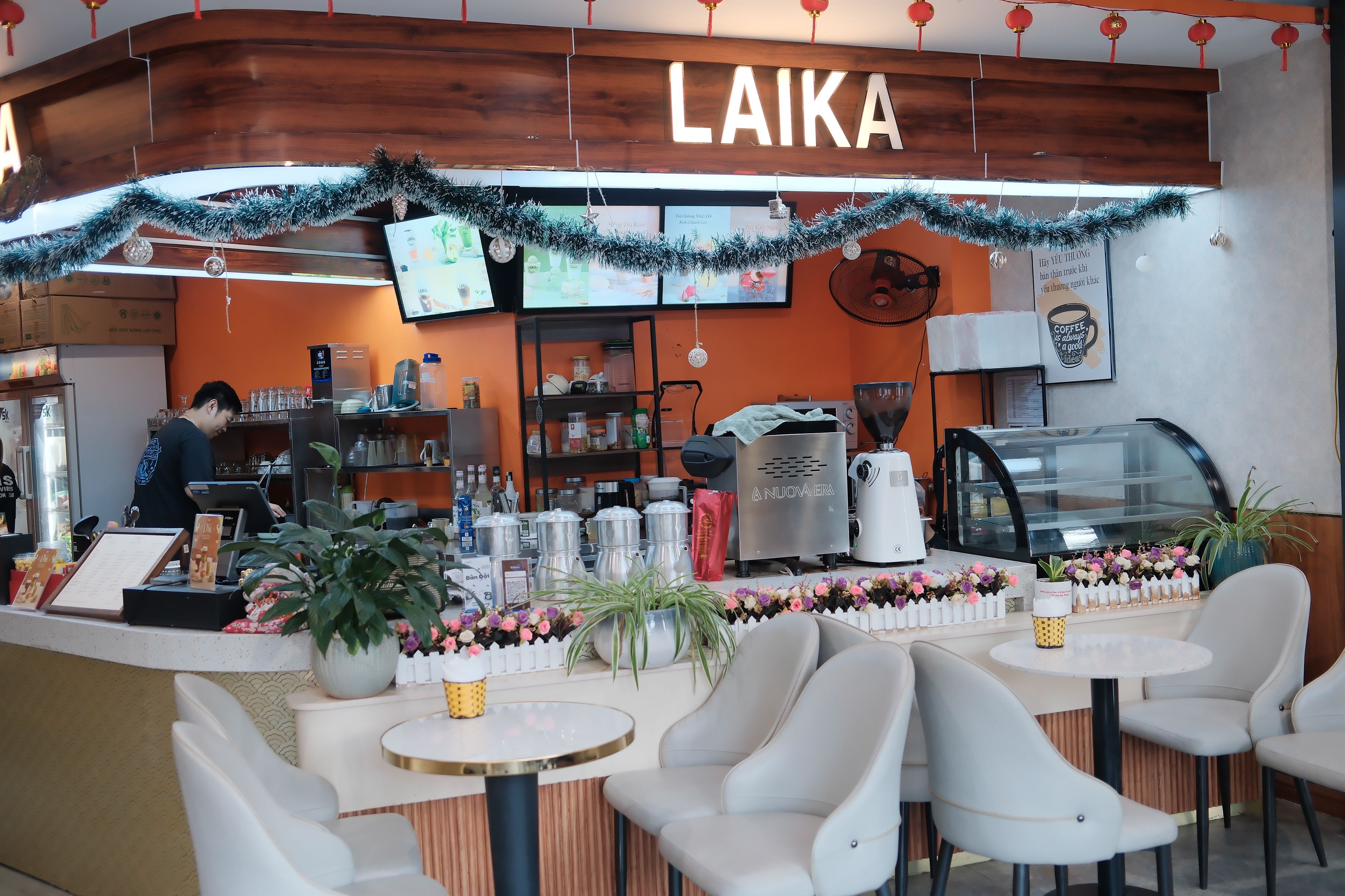 Interior de una cafetería con mostrador, zona de estar y un panel con la carta.