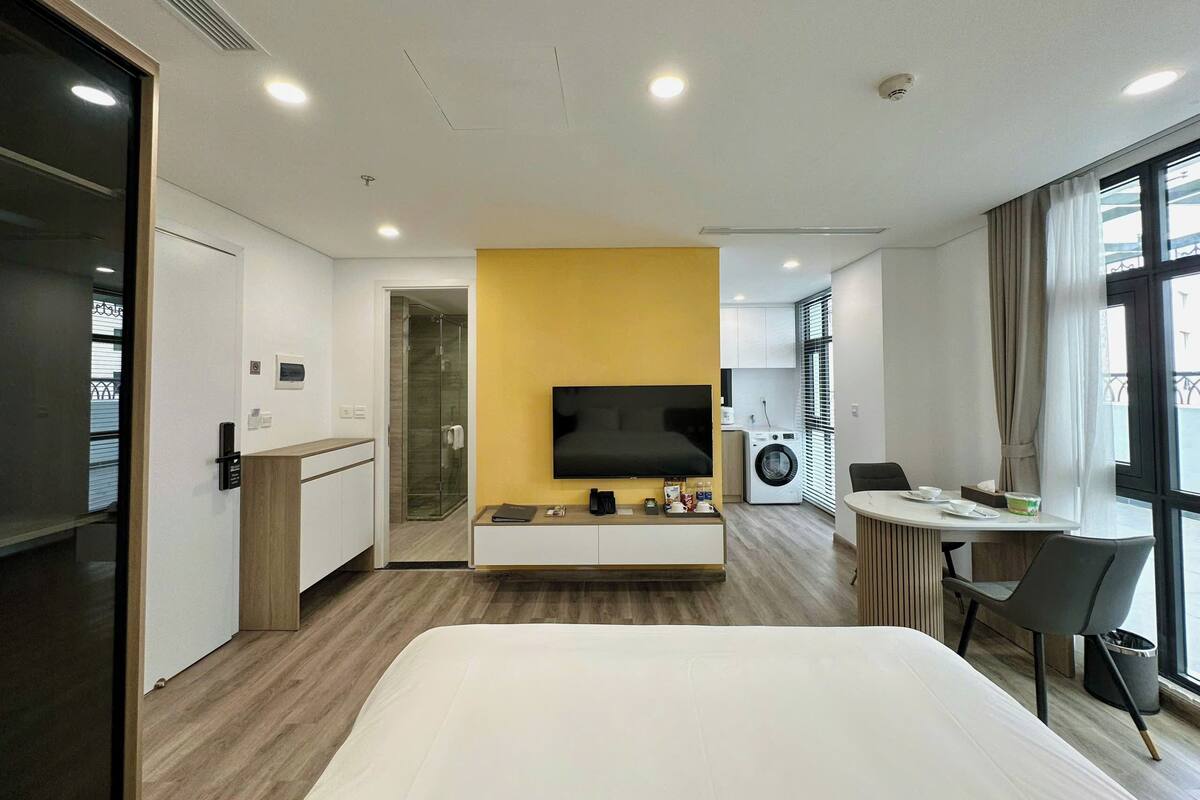 A hotel room with a bed, a TV, a washing machine, a dining area, and a shower.