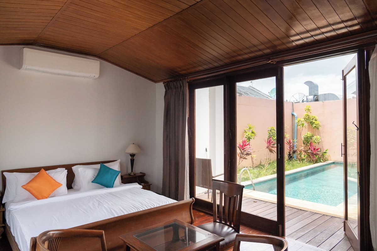 Una habitación de hotel con cama, una mesita, una silla, una ventana y vista a una piscina.