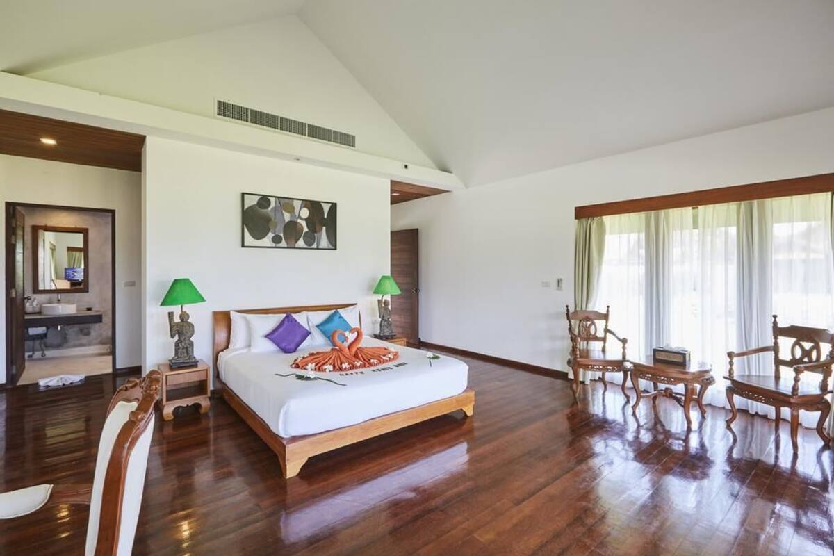 Amplia habitación de hotel con una cama grande, piso de madera, dos lámparas de noche, un cuadro en la pared y vistas al exterior a través de un ventanal.