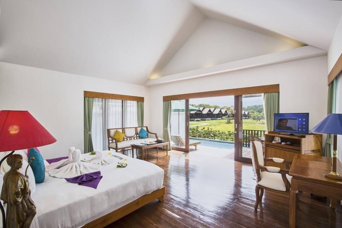 Una habitación amplia con cama, escritorio, televisión y vistas a una piscina y zonas verdes.