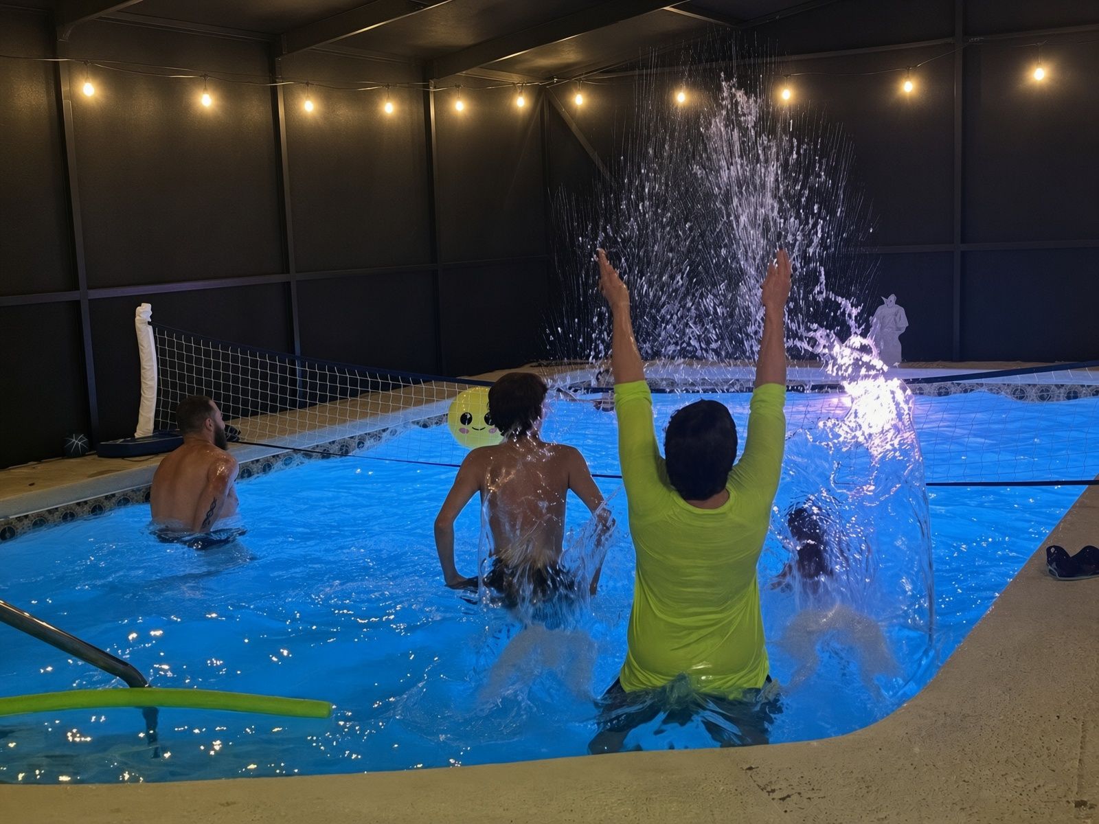 An indoor swimming pool with a netted area, water jets, and a person raising their arms.