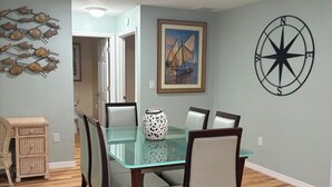 En matplats med ett glasbord, trästolar, en dekorativ väggdekoration i form av fiskar, en kompass som väggdekoration och en inramad tavla.