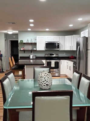 A modern kitchen with white cabinets, stainless steel appliances, and a glass dining table with chairs. - Captain's Corner, 4/2 w/Heated Pool & 4 kayaks Waterfront Canal Weeki Wachee (Spring Hill)