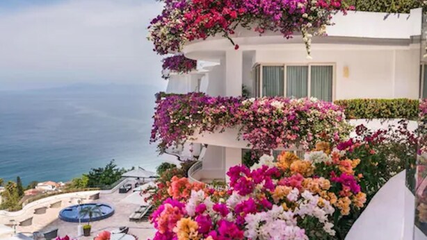 Ein mehrstöckiges Gebäude mit Balkonen, die mit Blumen geschmückt sind, einem Pool und Blick auf das Meer.