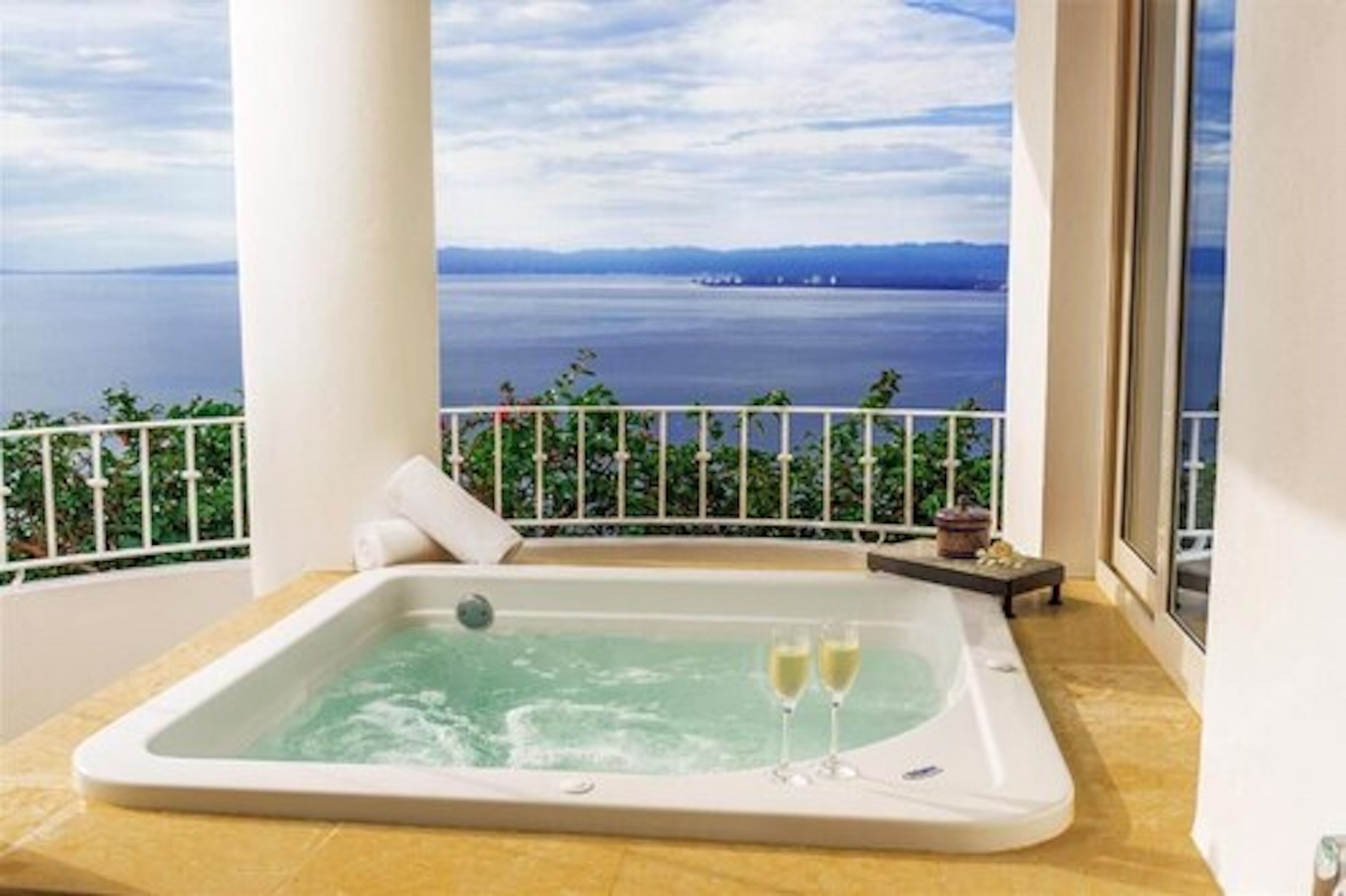 Un balcon avec un jacuzzi, deux coupes de champagne et une vue sur la mer.