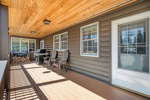 Eine überdachte Veranda mit Grill, Stühlen und einem Holzstoß.