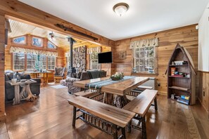 Ein gemütliches Blockhaus-Interieur mit einem Holzesstisch, Bänken, einem Kamin und einem Fernseher.