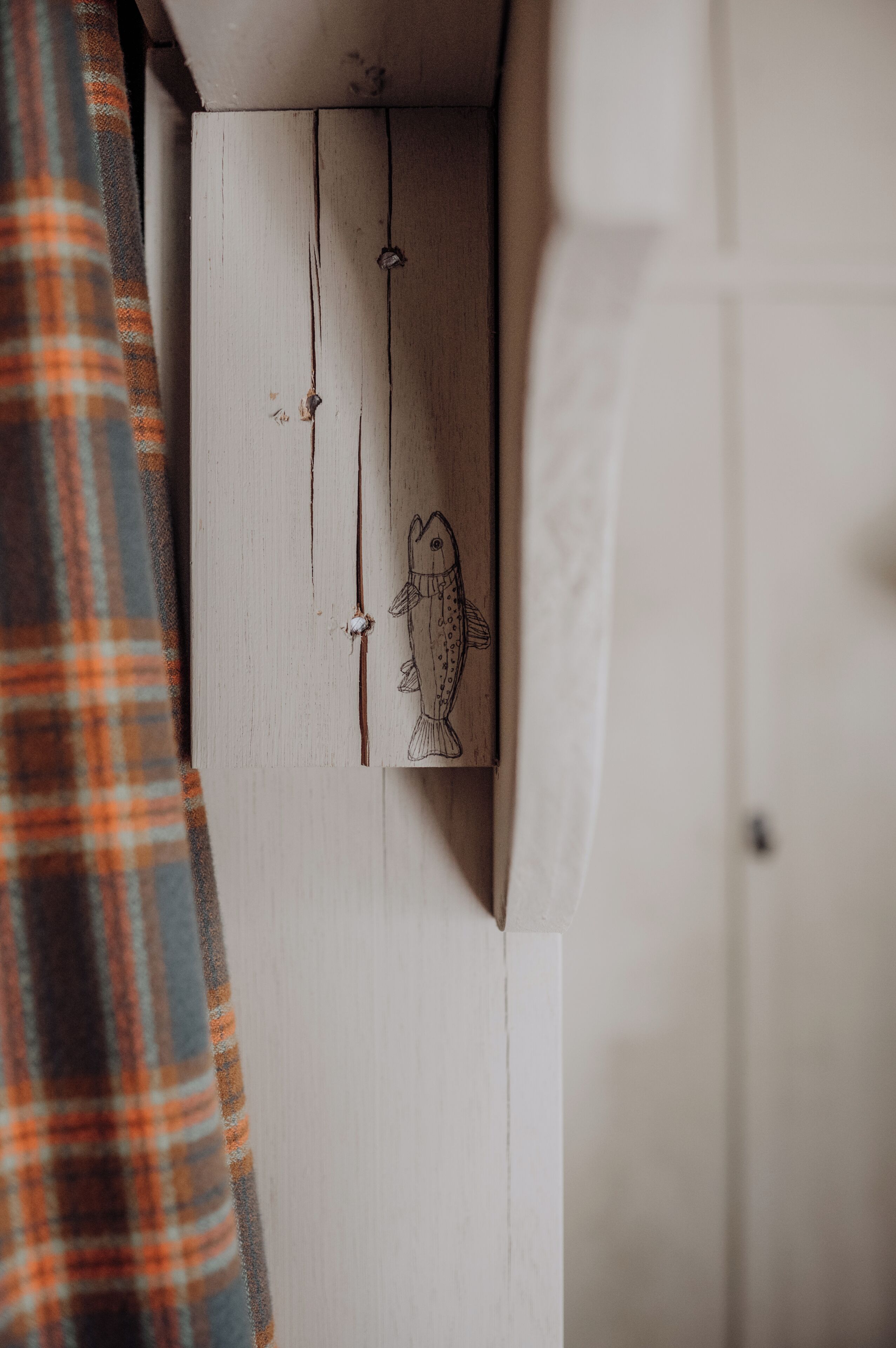 Ein Holzkabinett mit einem Fischgemälde, einem Karomuster-Vorhang und einer weißen Wand.