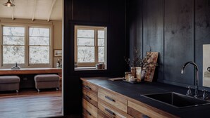 A modern kitchen with wooden cabinets, a black countertop, and a sink. There are two windows with a view of trees outside.
