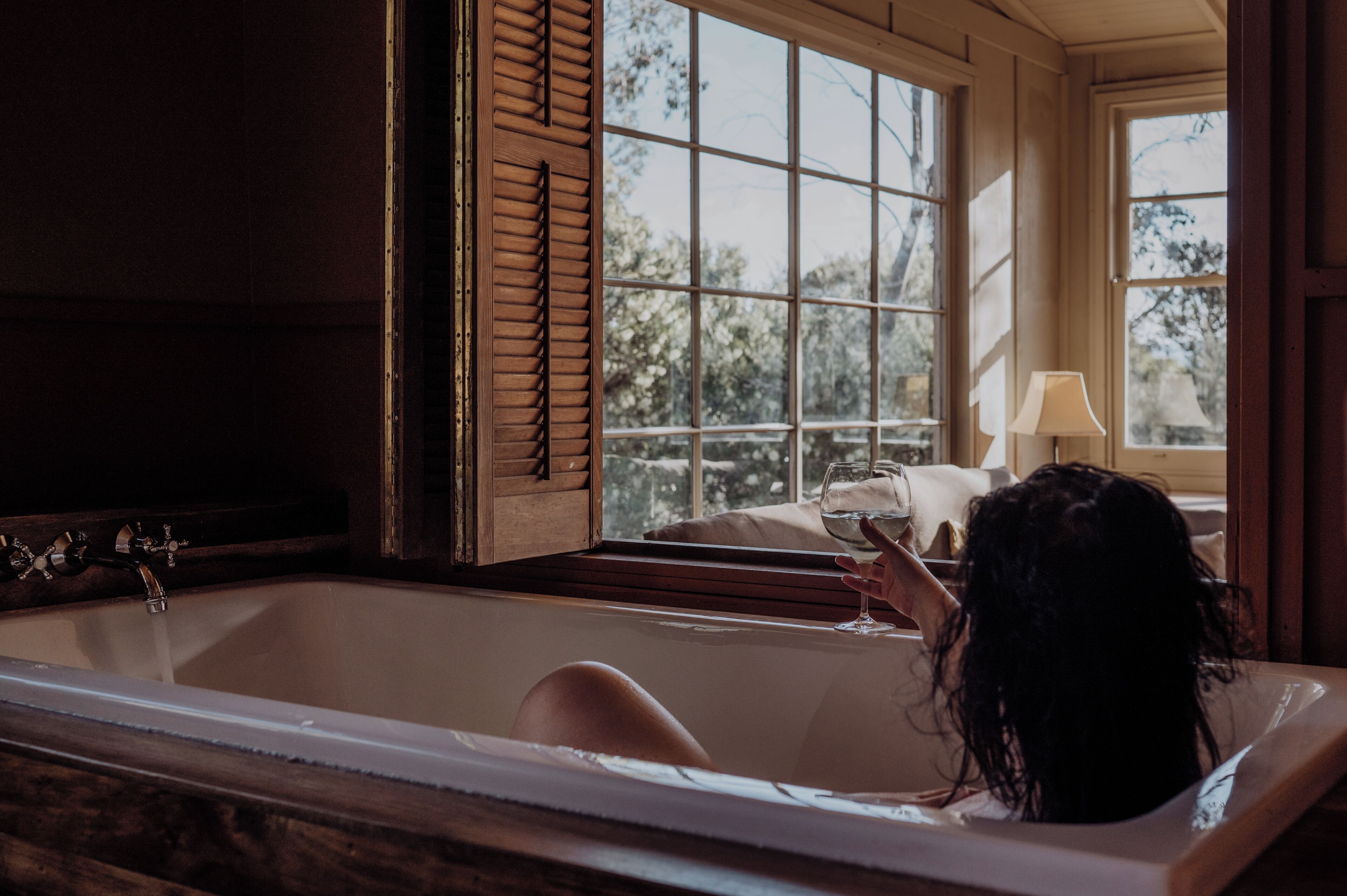 A bathtub with a window, a lamp, and a view of trees outside.