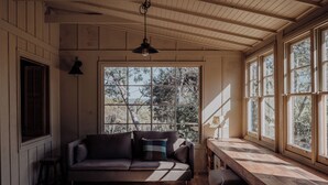 A room with a wooden ceiling, a sofa, a bench, and large windows with a view of trees.