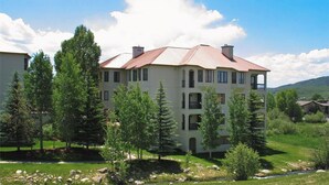 A multi-story building with a red roof, surrounded by trees and a grassy area. - Peaceful Retreat, Pool&Hot Tub, Walk to Village, Private Shuttle, Bike Anywhere! (Steamboat Springs)
