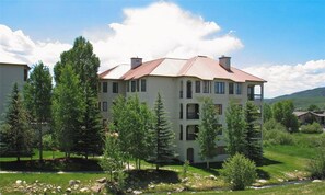 A multi-story building with a red roof, surrounded by trees and a grassy area. - Peaceful Retreat, Pool&Hot Tub, Walk to Village, Private Shuttle, Bike Anywhere! (Steamboat Springs)