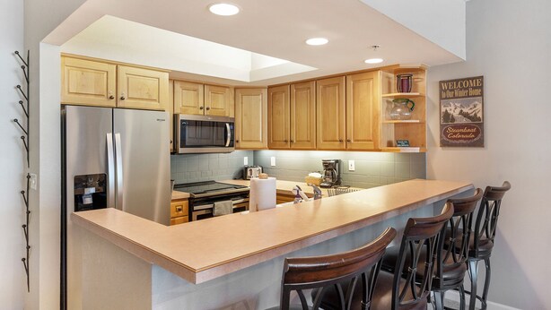 A modern kitchen with wooden cabinets, stainless steel appliances, and a bar area with stools. - Peaceful Retreat, Pool&Hot Tub, Walk to Village, Private Shuttle, Bike Anywhere! (Steamboat Springs)