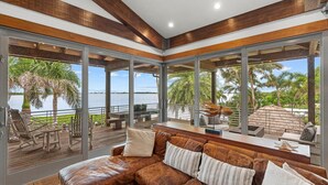 Un salon moderne doté d’une grande fenêtre, d’un plafond en bois et offrant une vue sur une étendue d’eau.