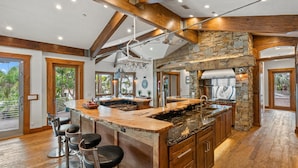 Une cuisine spacieuse avec un grand îlot central, des éléments décoratifs en pierre et des poutres en bois.