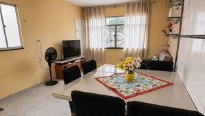 A dining area with a table, chairs, a fan, a TV, and a window with curtains. - Casa confortável (Belém)