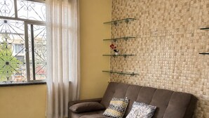 A living room with a sofa, a coffee table, a window with curtains, and a patterned wall. - Casa confortável (Belém)