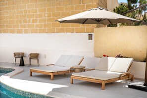A poolside area with lounge chairs, a table, and an umbrella. - Casa Elana Holiday Gozitan Home, Xagħra Gozo, Malta (Xagħra Gozo)
