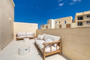 Eine Dachterrasse mit zwei Sofas und einem runden Tisch, umgeben von einer hohen Mauer und Gebäuden im Hintergrund.
