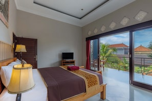 Habitación de hotel con cama, televisión, lámpara y balcón con vistas al exterior.