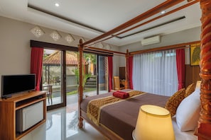 Habitación de hotel con cama con dosel, televisor y vista a un jardín a través de la puerta corrediza de vidrio.