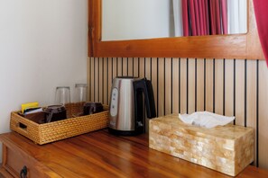 A wooden table with a woven basket containing bottles, a kettle, and a tissue box. - Puri Bisma Ubud (Ubud)