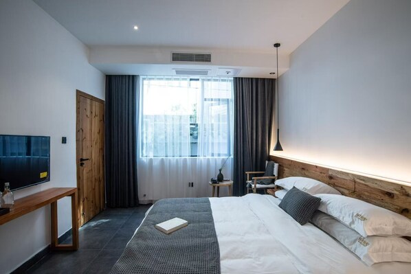 Habitación de hotel moderna con cama, mesita de noche, lámpara y vistas al exterior.