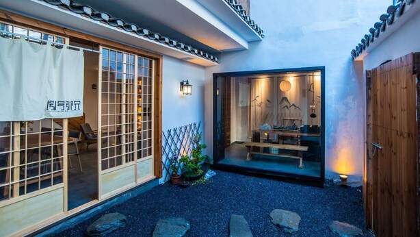 A traditional Japanese building with a wooden exterior, a sliding glass door entrance, and a small outdoor seating area with a table and chairs. - Fenghuang Bahaobieyuan (Xiangxi)