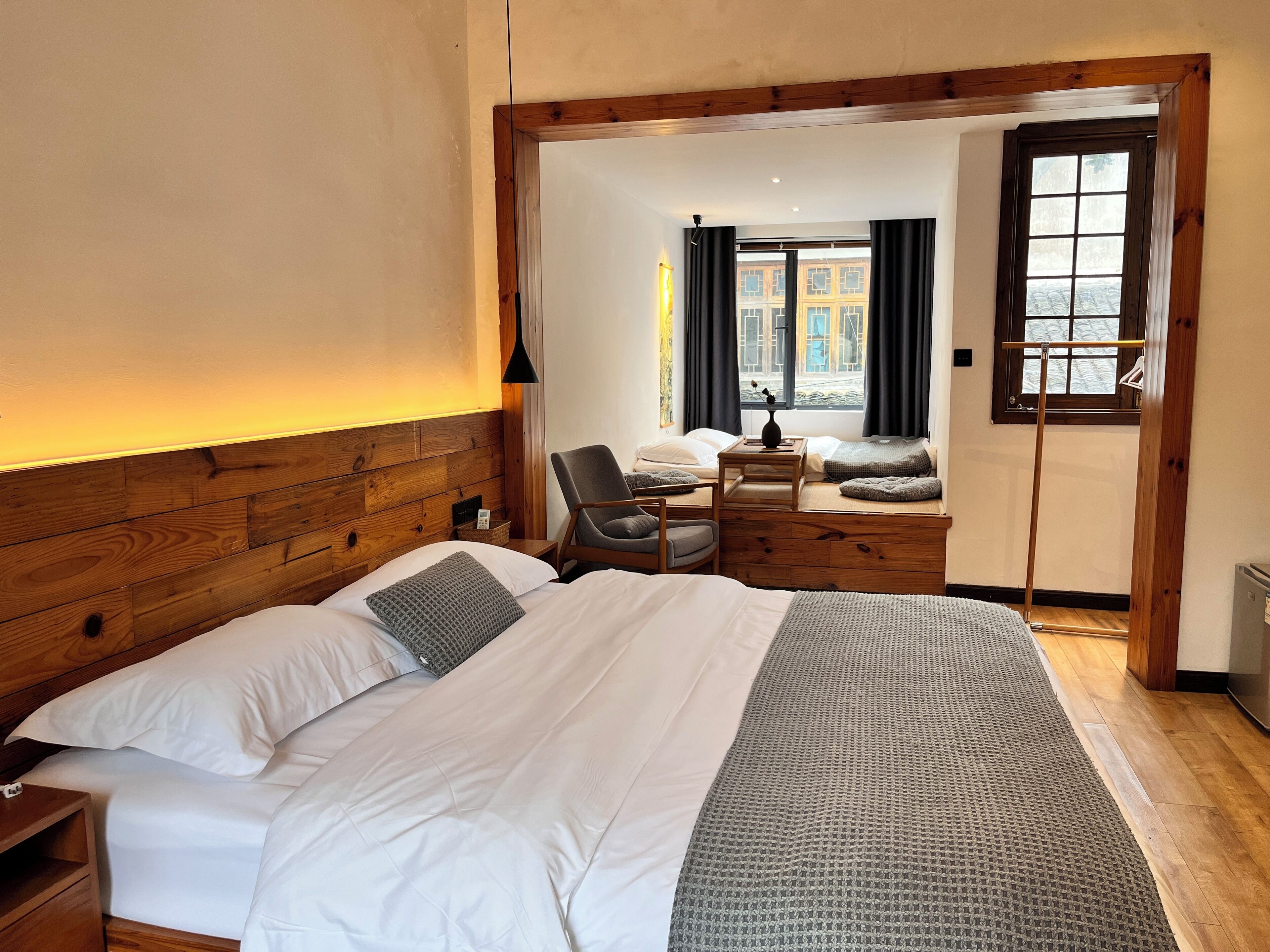 Un dormitorio con cabecera de madera, una cama con ropa blanca, un escritorio con silla y vistas por una puerta abierta.